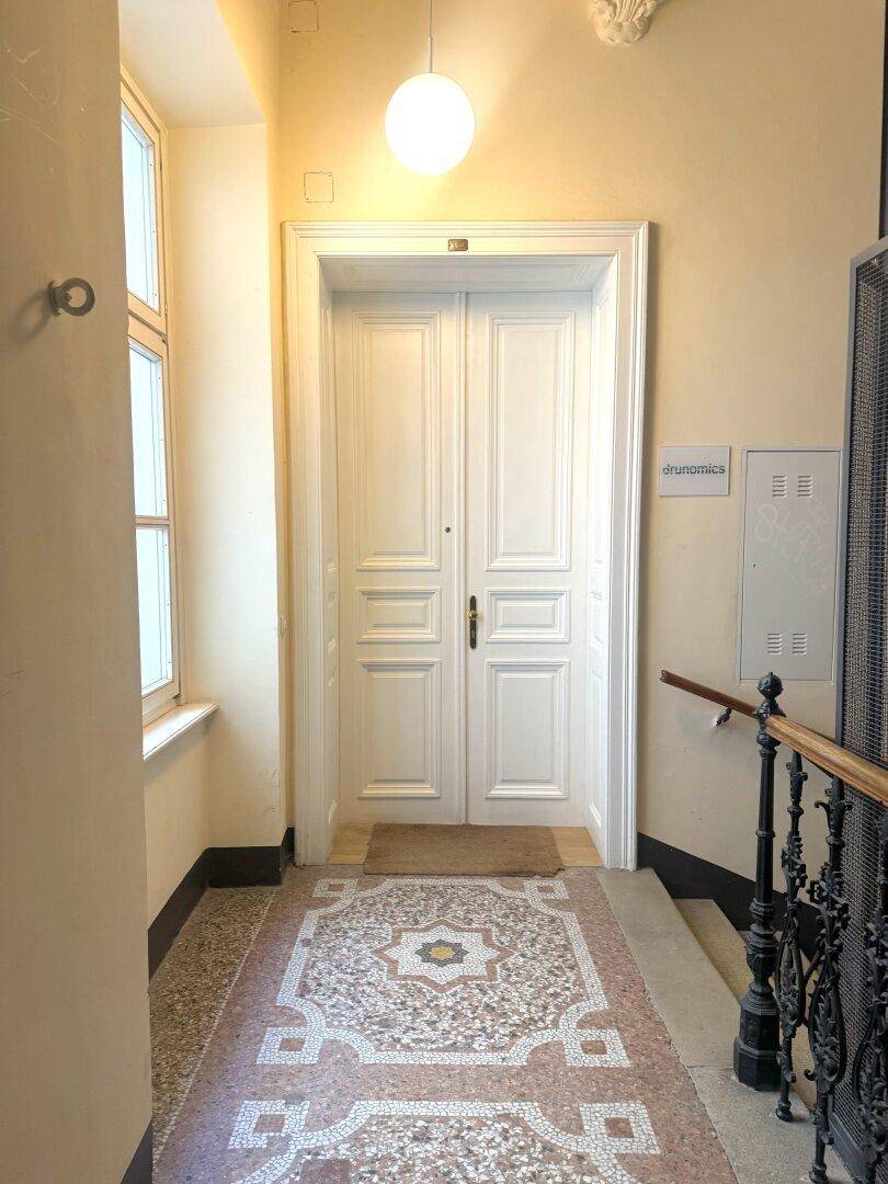 Historischer Eingangsbereich mit gemustertem Terrazzoboden und einer großen Doppeltür zur Wohnung.