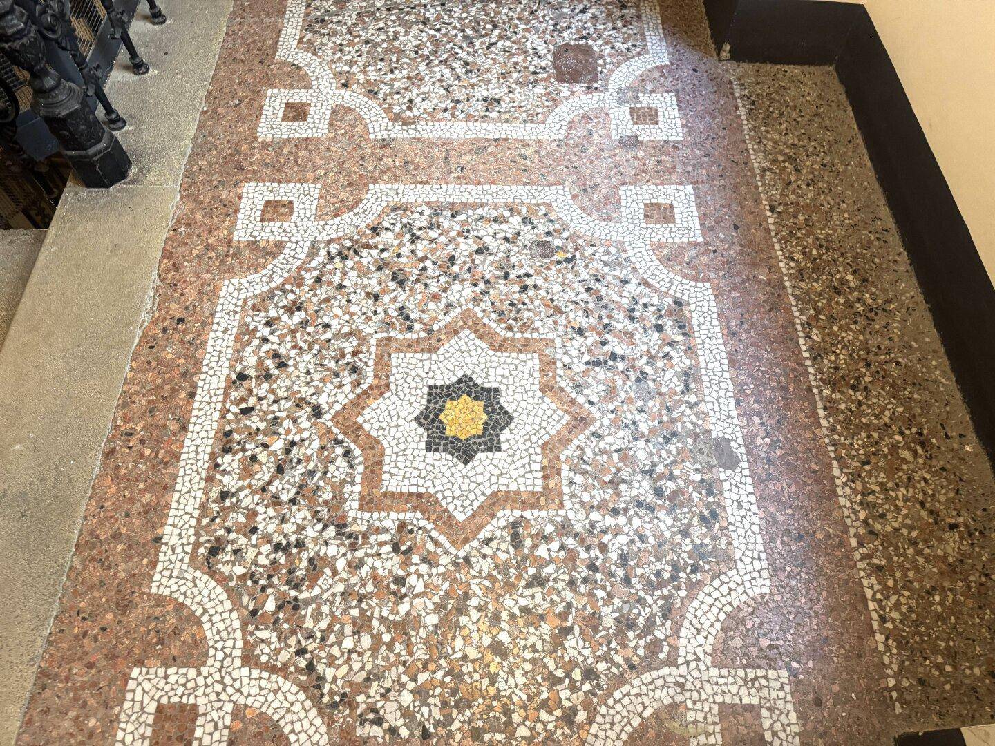 Detailaufnahme des kunstvollen Terrazzobodens im Eingangsbereich mit geometrischen Mustern und Farben.