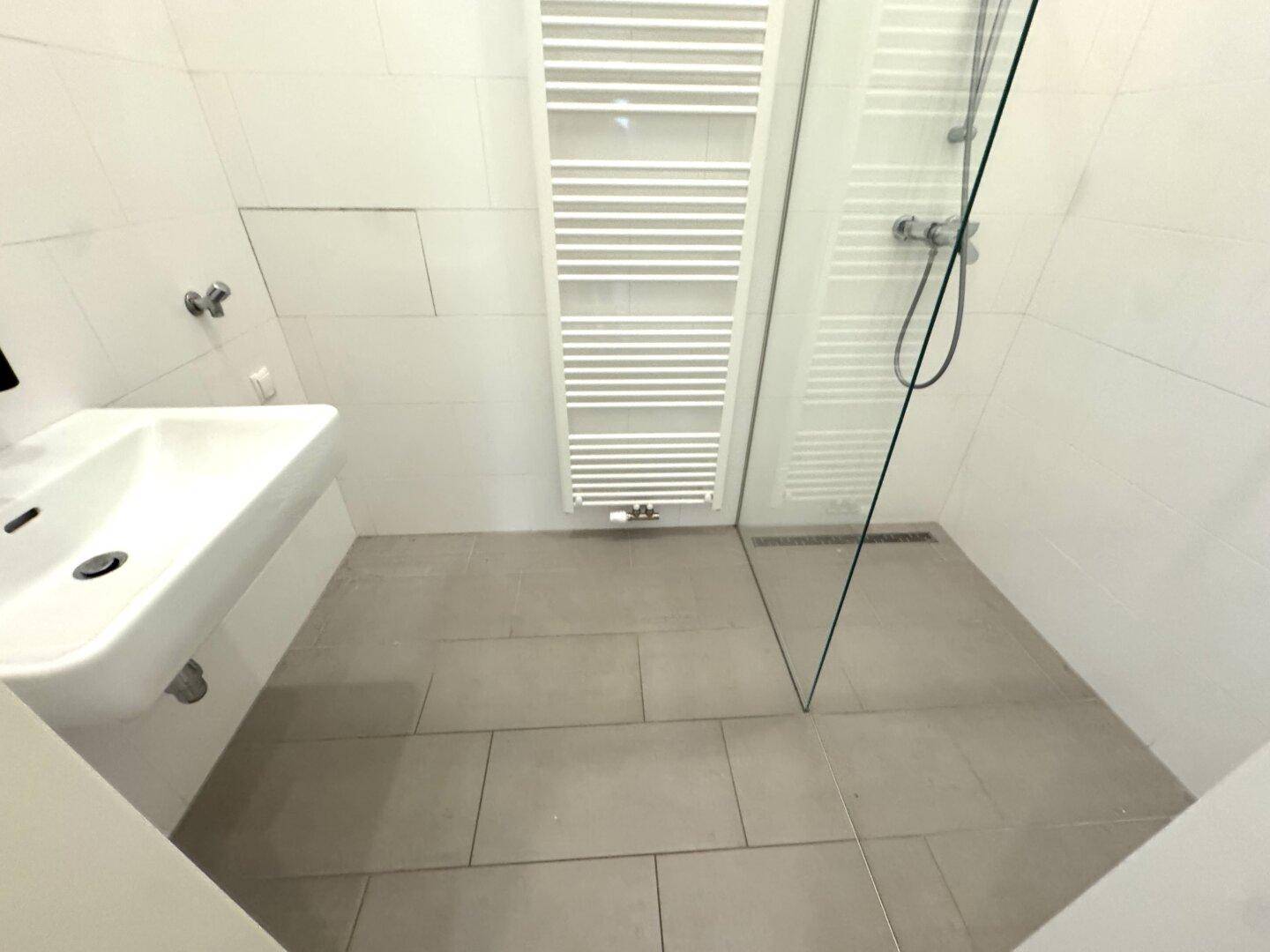 Modernes Badezimmer mit ebenerdiger Dusche, weißer Wandverkleidung und praktischem Handtuchheizkörper.