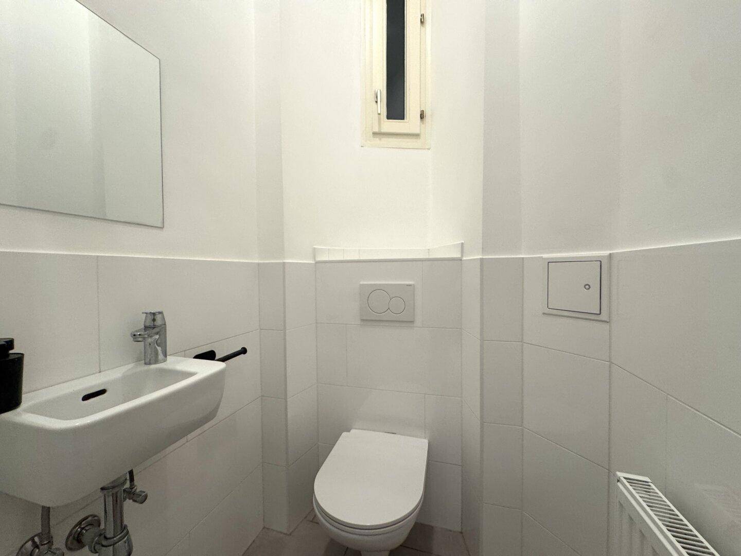 Kleines Gäste-WC mit wandhängendem WC, Waschbecken und einem schmalen Fenster für Tageslicht.