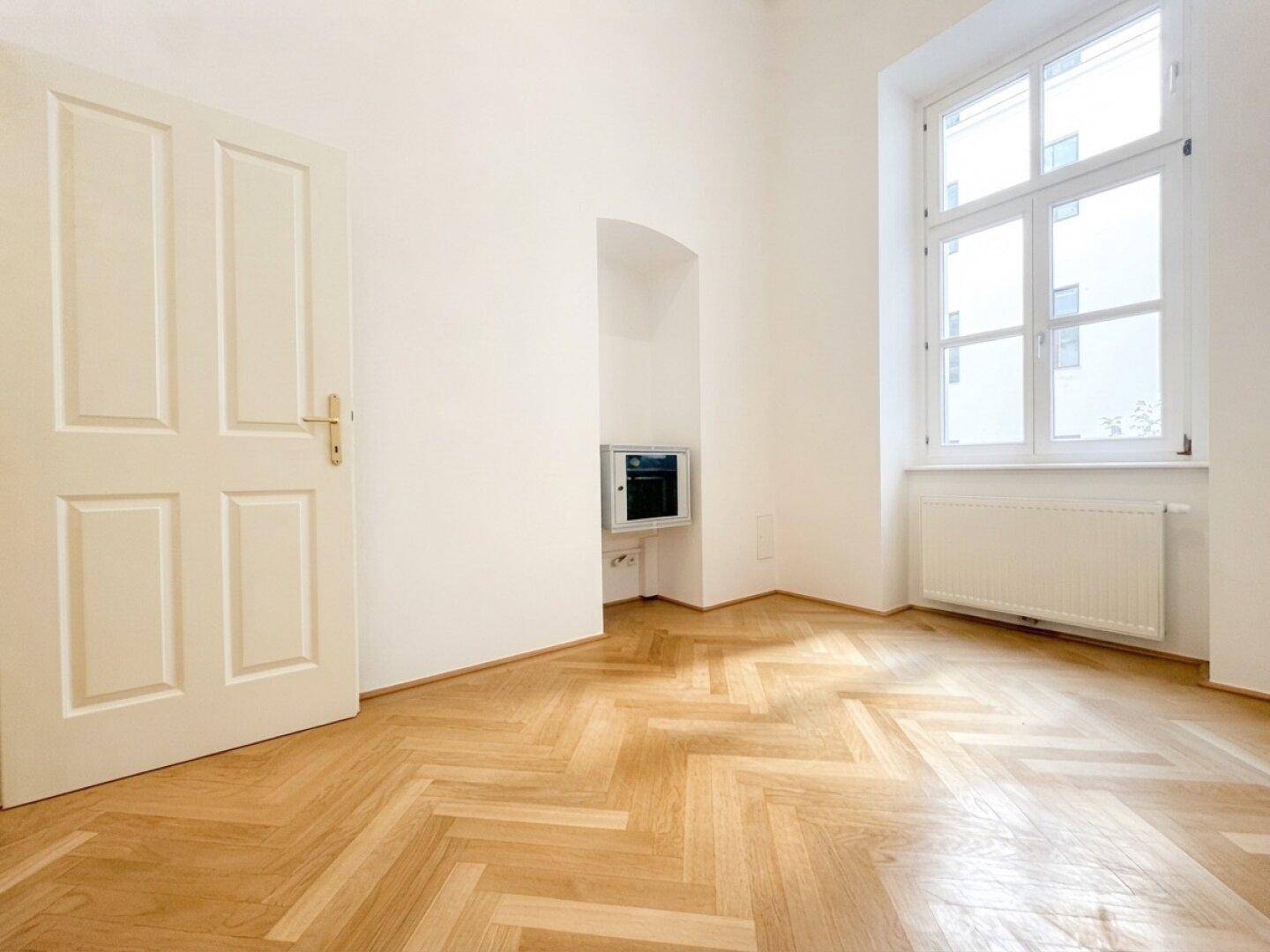 Heller Raum mit Fischgrätparkett, einem großen Fenster und einer praktischen Nische in der Wand.