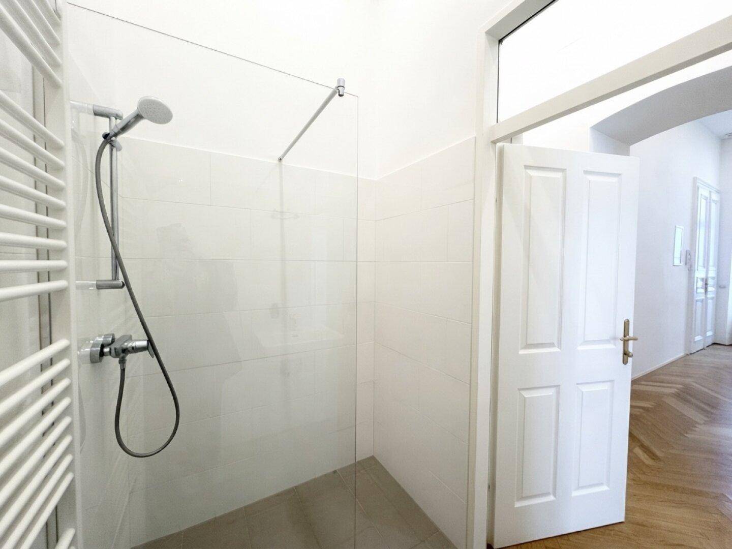 Ebenerdige Dusche mit Glasabtrennung und moderner Armatur in einem hellen, gefliesten Badezimmer.