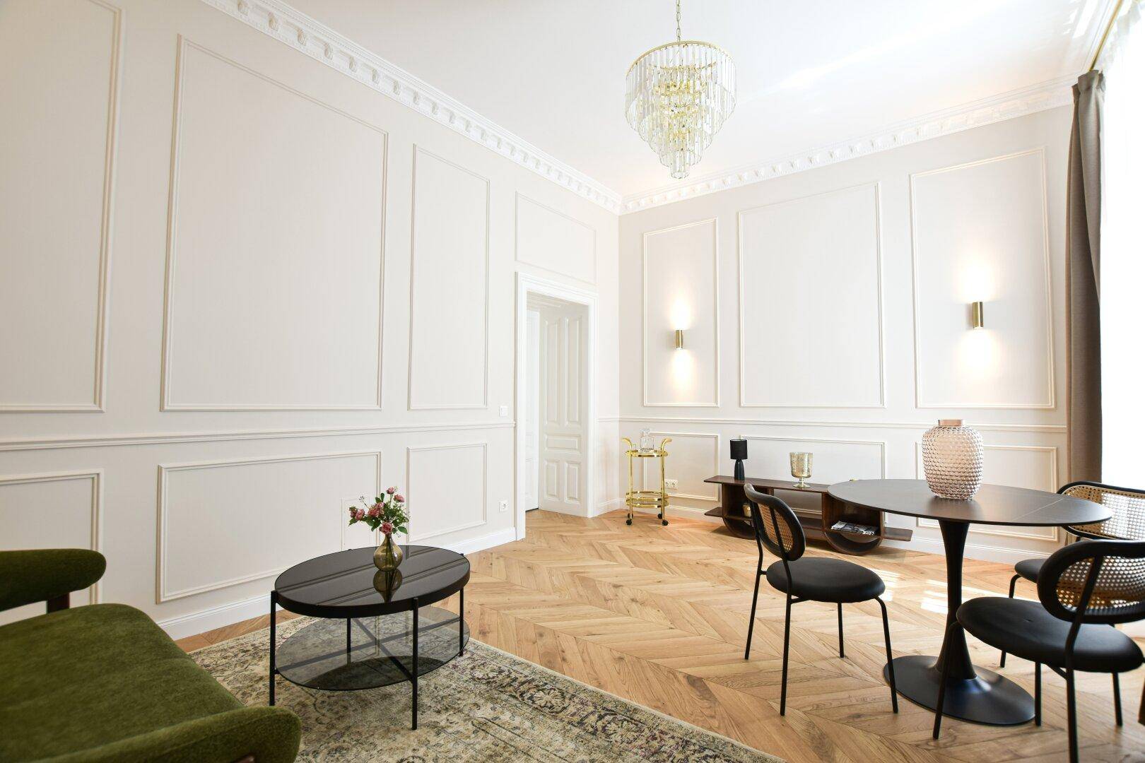 Geräumiges Wohnzimmer mit eleganten Wandpaneelen, Fischgrätparkett und Kronleuchter.