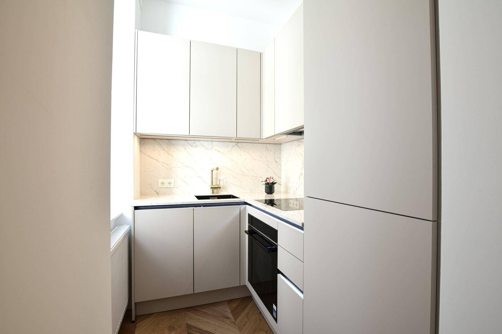 Moderne, kompakte Küche mit weißen Schränken, integrierten Geräten und Fischgrätparkett.