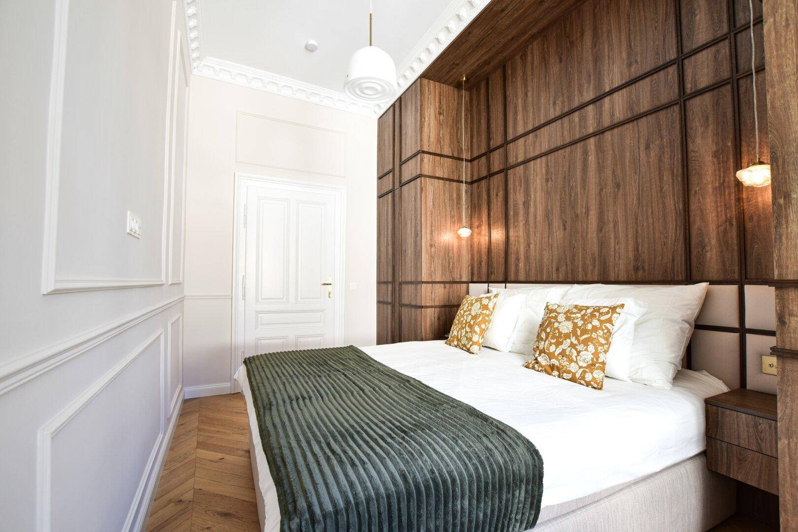 Schlafzimmer mit Holzwandverkleidung, Fischgrätparkett und dekorativen Kissen.