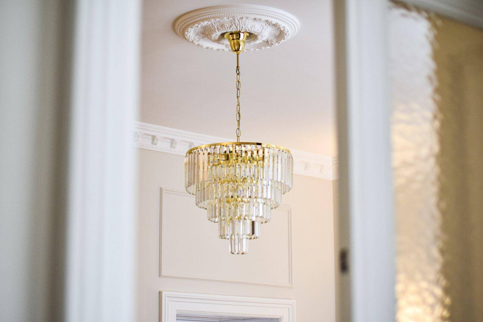 Detailaufnahme eines eleganten Kronleuchters mit Stuckverzierung an der Decke.