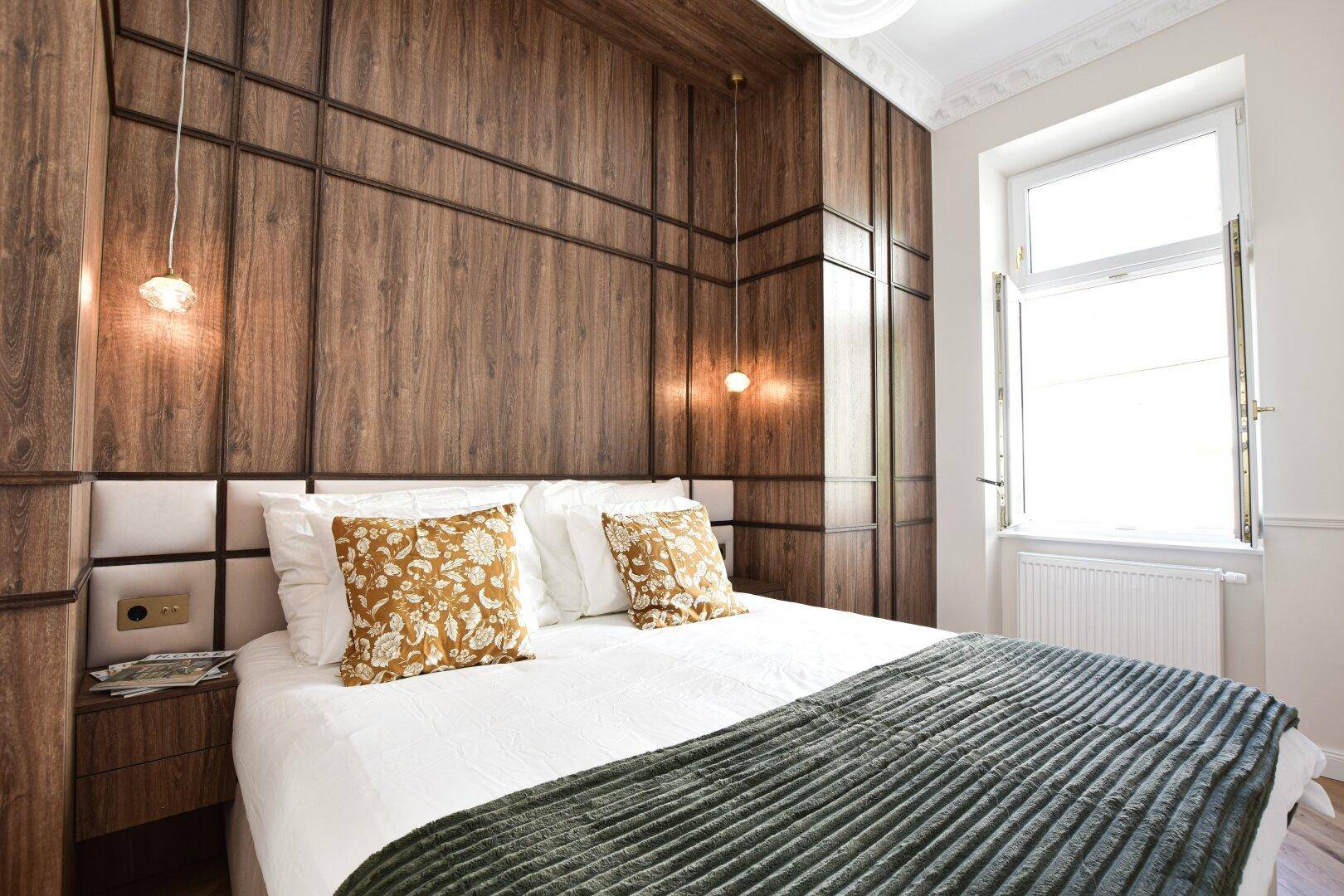 Helles Schlafzimmer mit Holzakzentwand, großem Fenster und bequemen Bett.