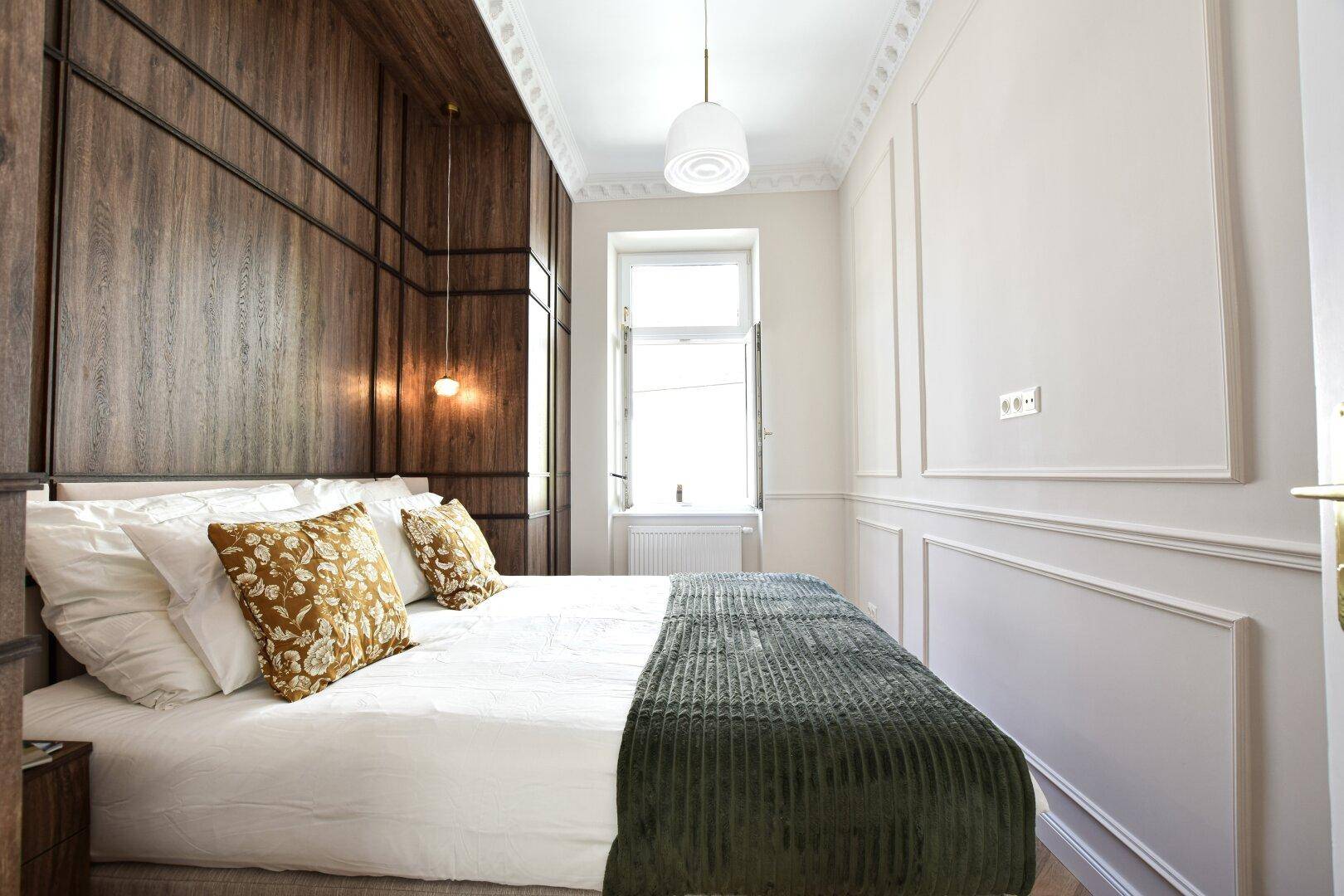 Schlafzimmer mit Holzwandverkleidung, Fischgrätparkett und eleganten Deckenleisten.