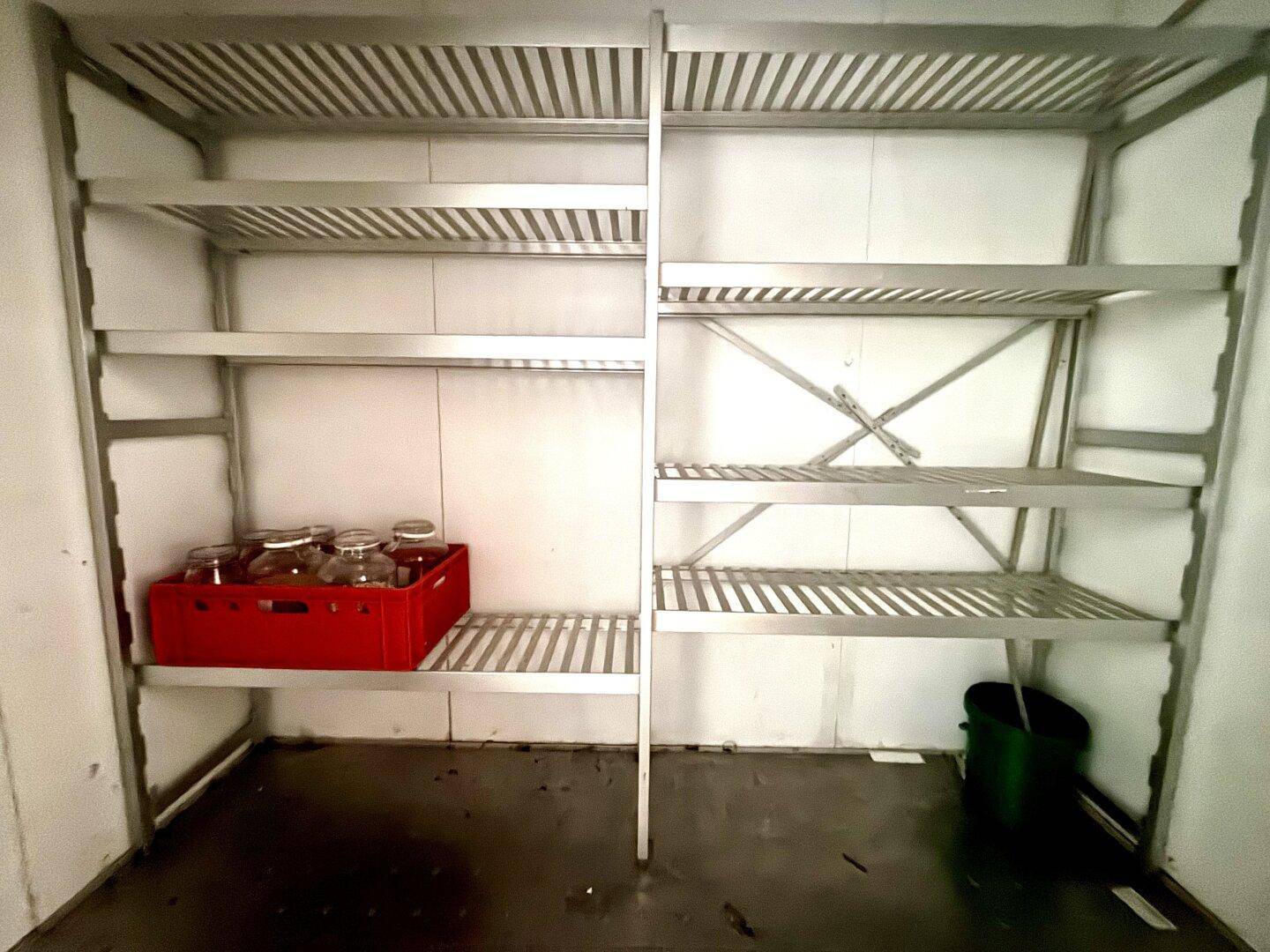 Begehbarer Kühlraum mit stabilen Metallregalen und einem roten Kasten auf dem Boden.