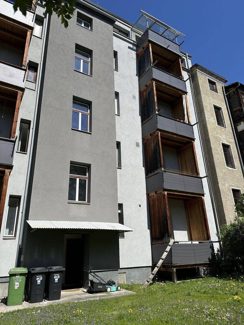 Fassade eines Mehrfamilienhauses mit Balkonen und einer kleinen Grünfläche im Vordergrund.
