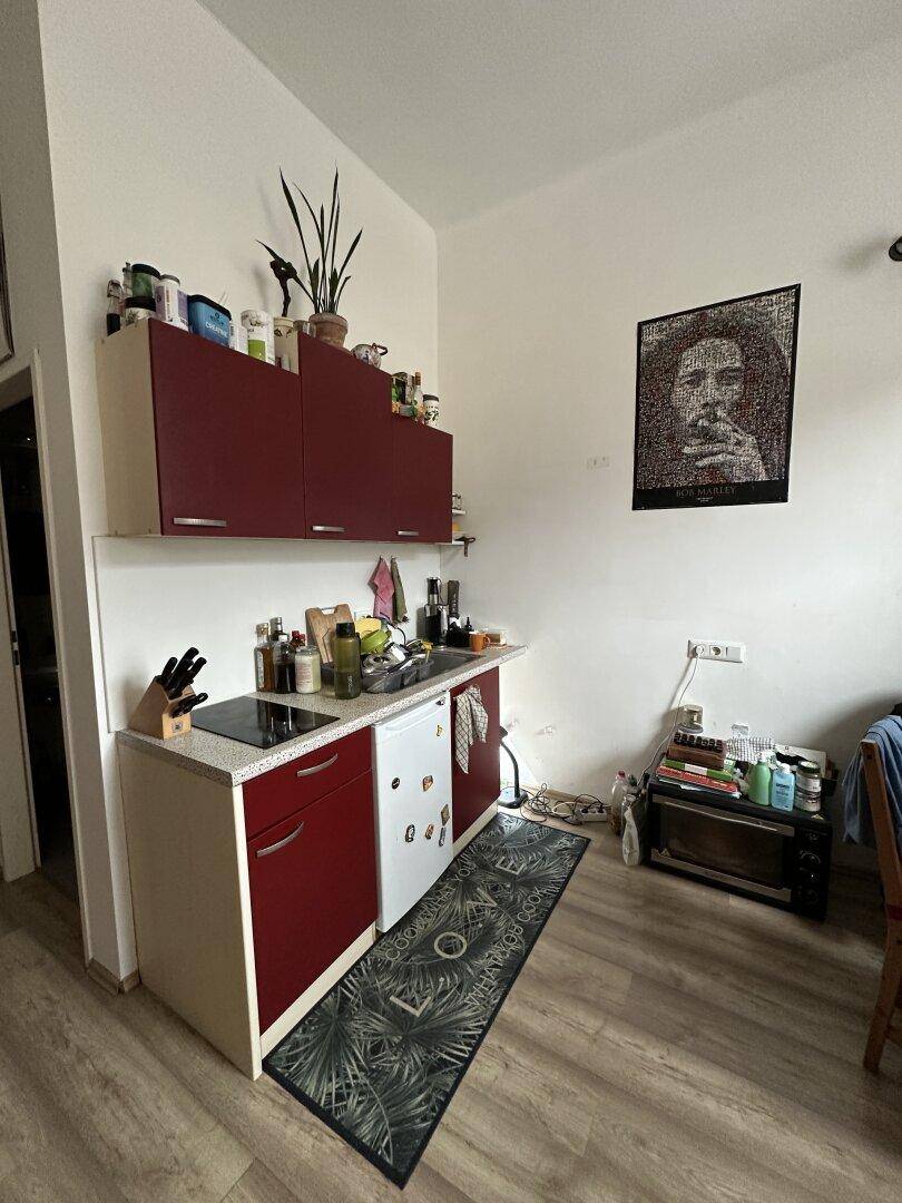 Kleine Küchenzeile mit roten Schränken, integriertem Kühlschrank und Kochfeld.