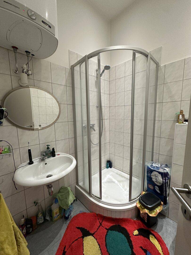 Badezimmer mit Eckdusche, Waschbecken und Boiler, gefliesten Wänden und Boden.