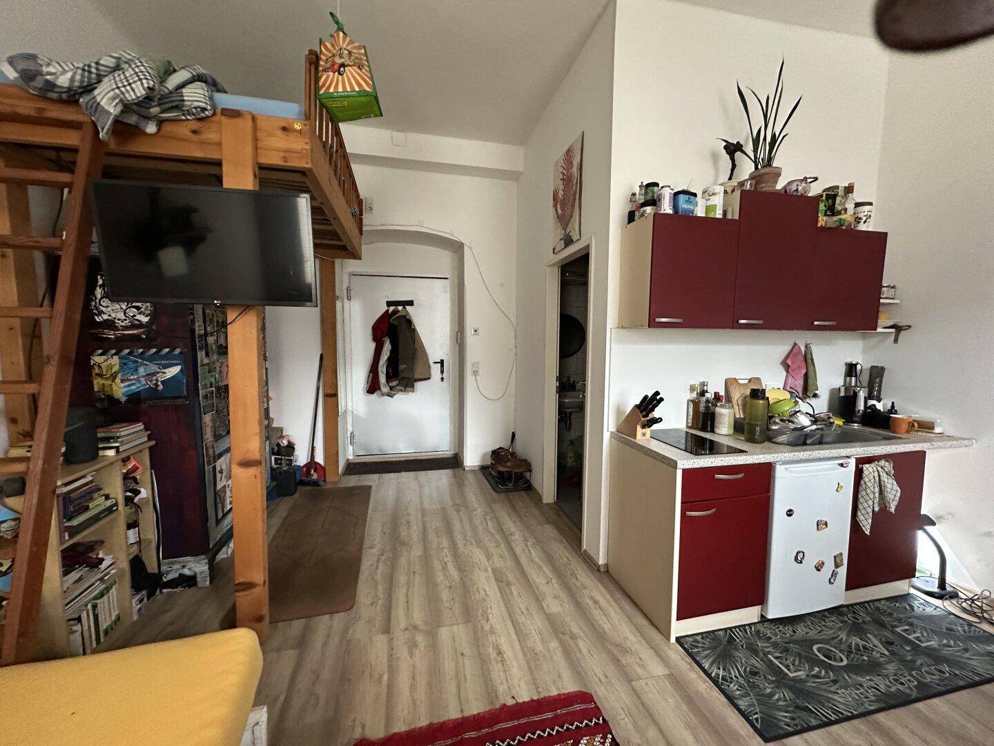 Kompakter Wohnbereich mit Hochbett, integrierter Küchenzeile und Laminatboden.
