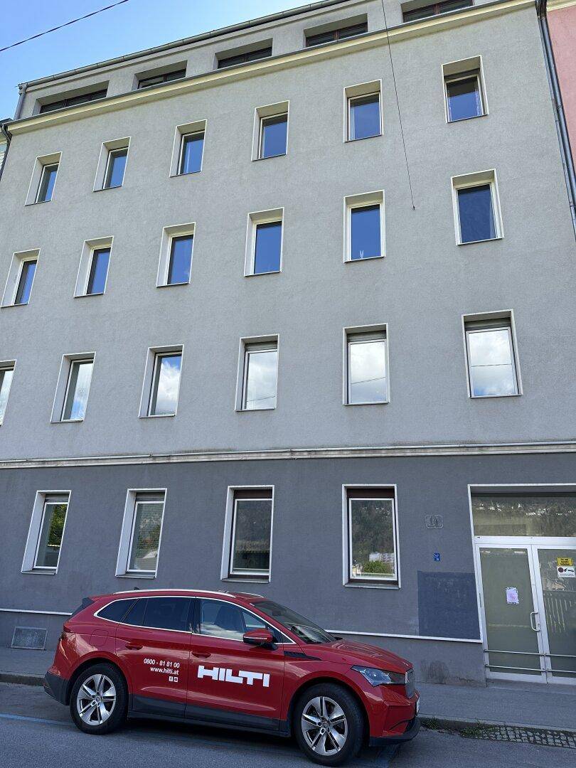 Straßenansicht eines mehrstöckigen Gebäudes mit vielen Fenstern und einem geparkten roten Auto.
