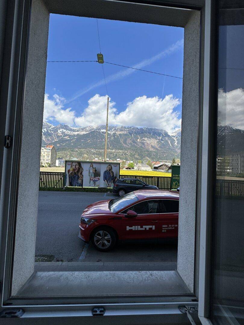 Blick aus dem Fenster auf eine Straße mit Auto und majestätische Berge im Hintergrund.