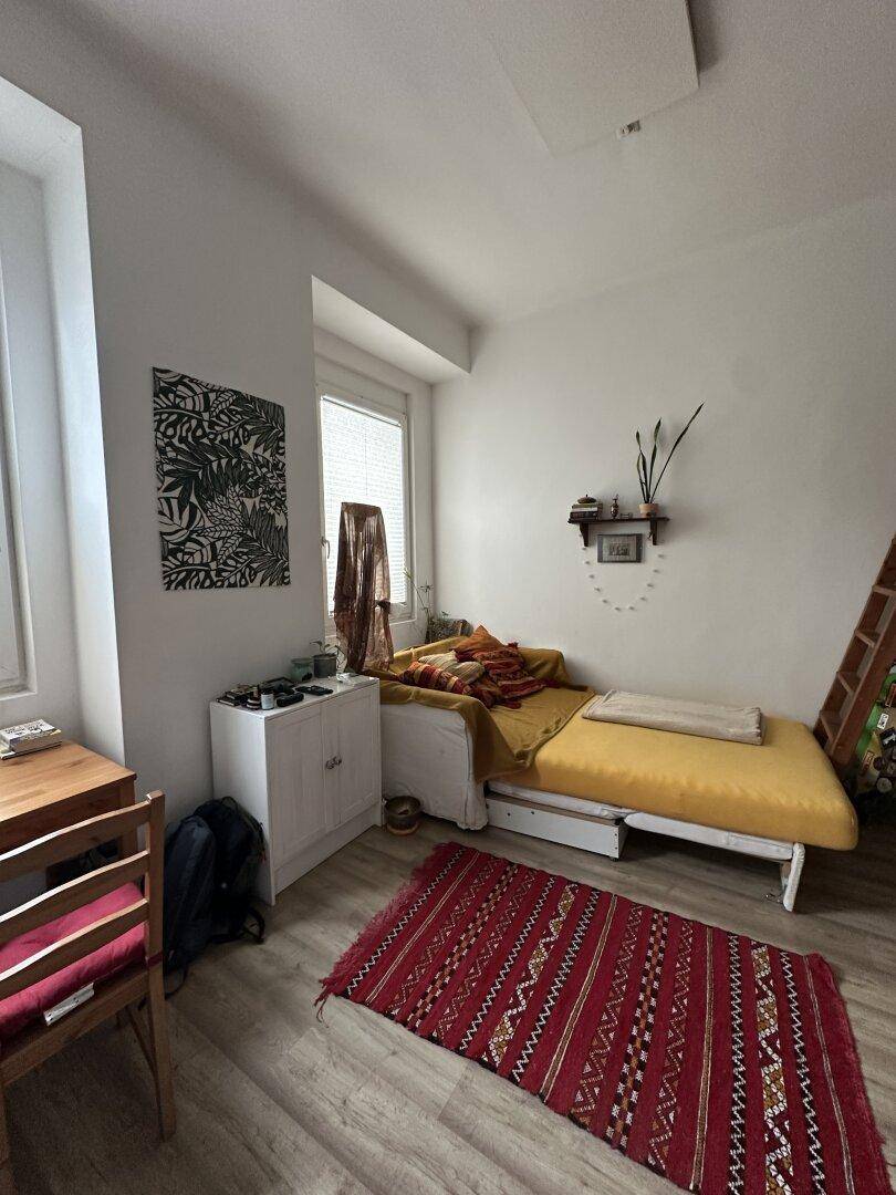 Helles Schlafzimmer mit Einzelbett, Schreibtisch und Fenster, ausgestattet mit Laminatboden.