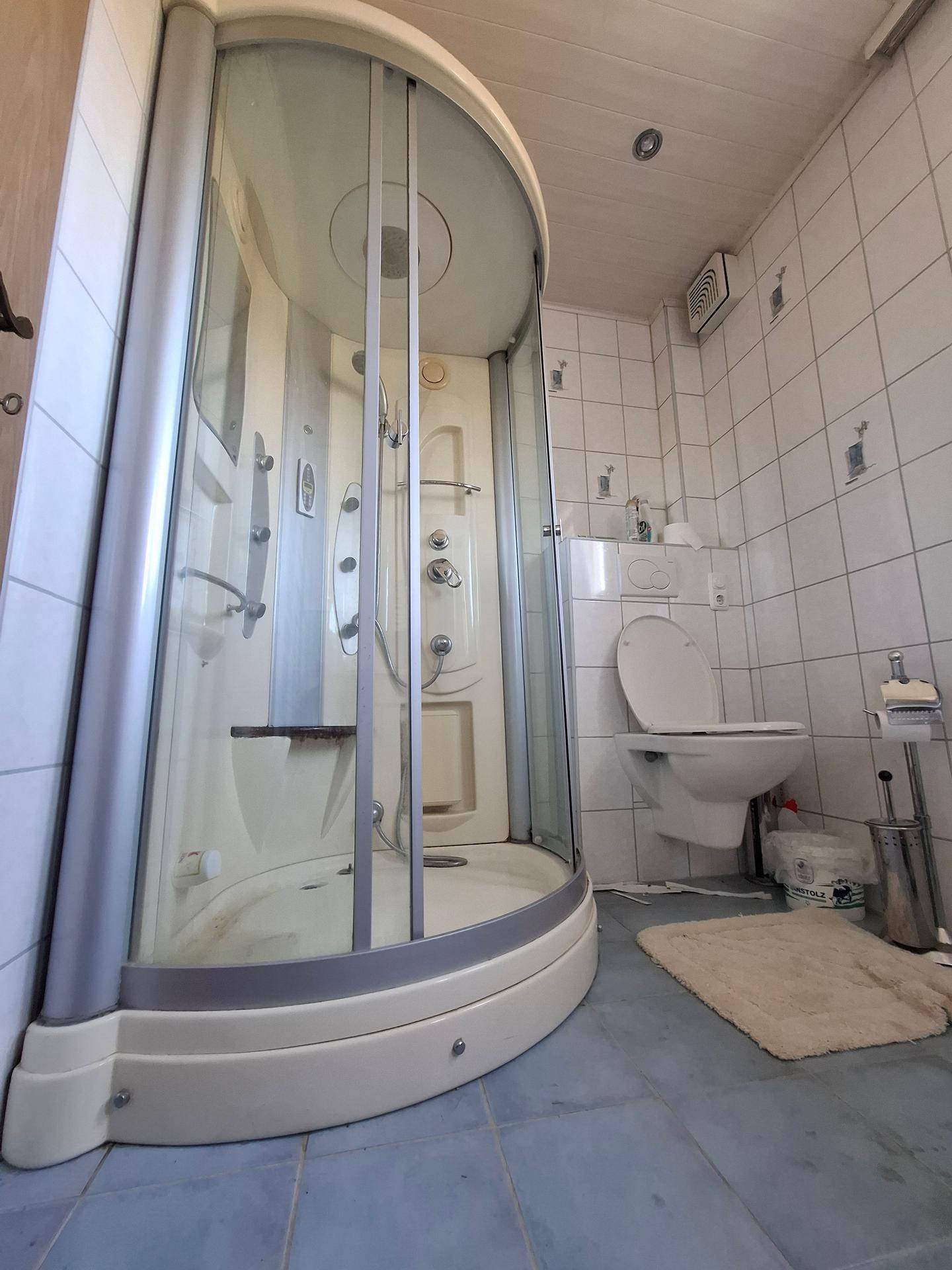 Badezimmer mit Duschkabine und WC, gefliest und mit Abluftventilator ausgestattet.