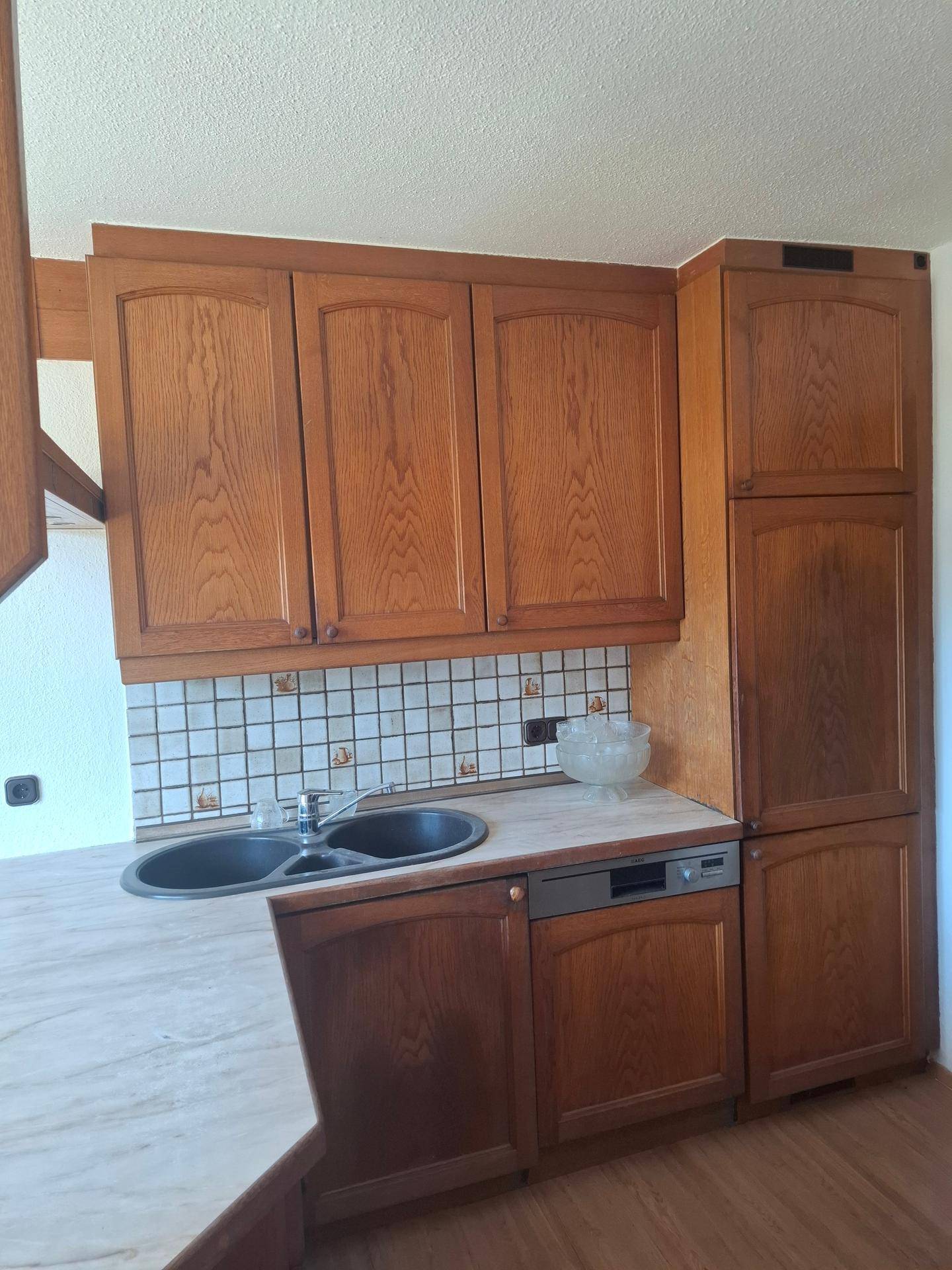 Traditionelle Holzküche mit dunkler Doppelspüle, Fliesenrückwand und integriertem Geschirrspüler.