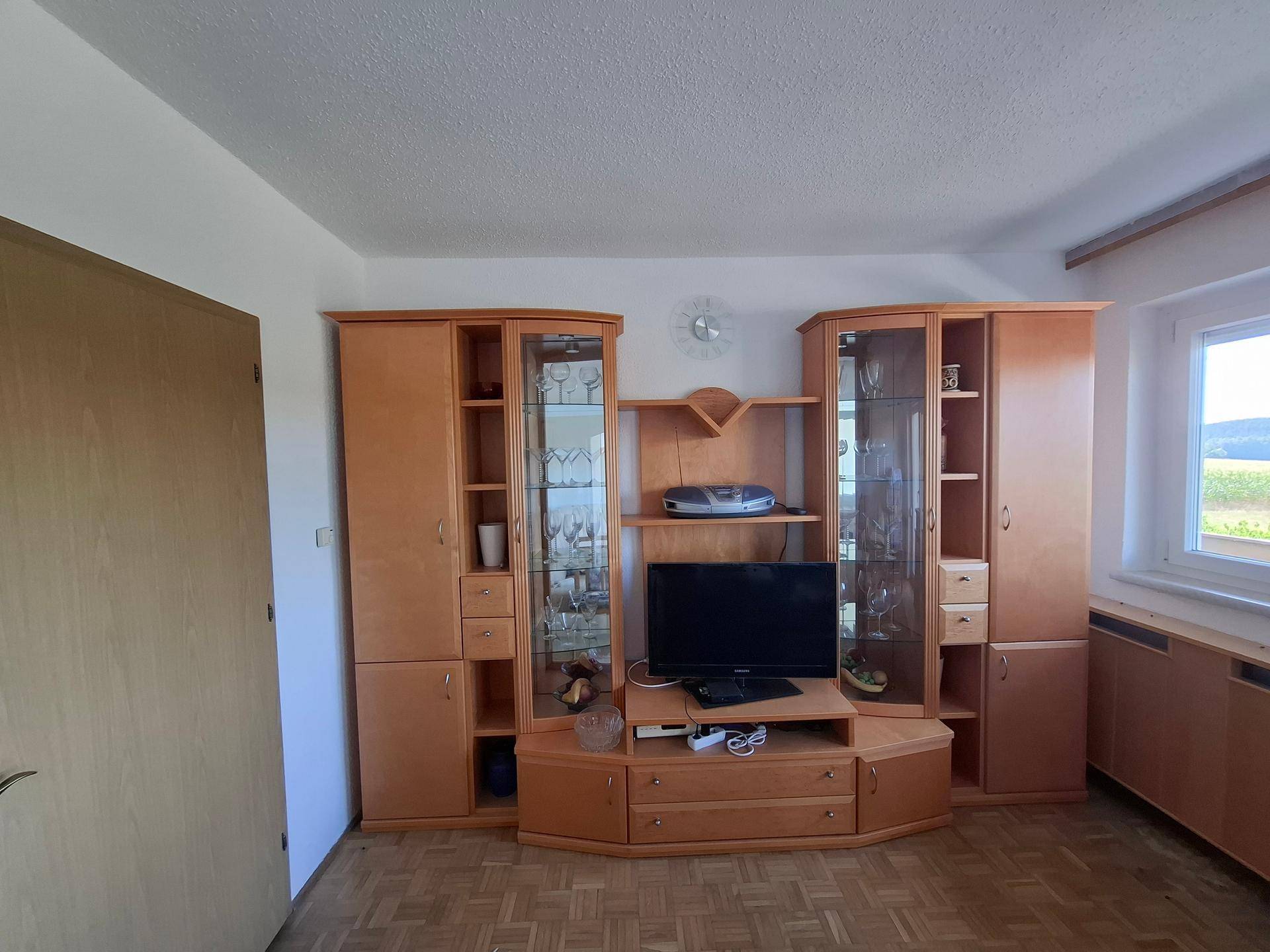 Wohnzimmer mit Holzschrankwand, Fernseher und Parkettboden, hell und funktional eingerichtet.
