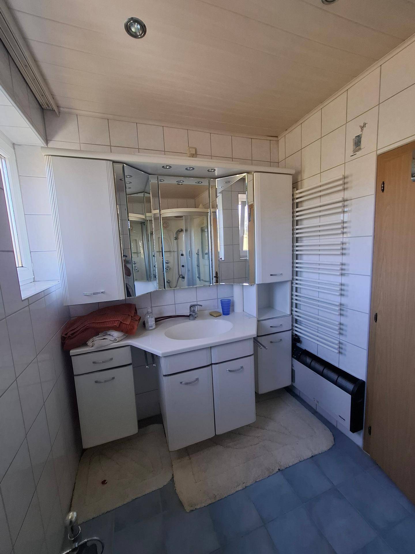 Badezimmer mit weißem Waschtisch, Spiegelschrank, beheiztem Handtuchhalter und Fenster.