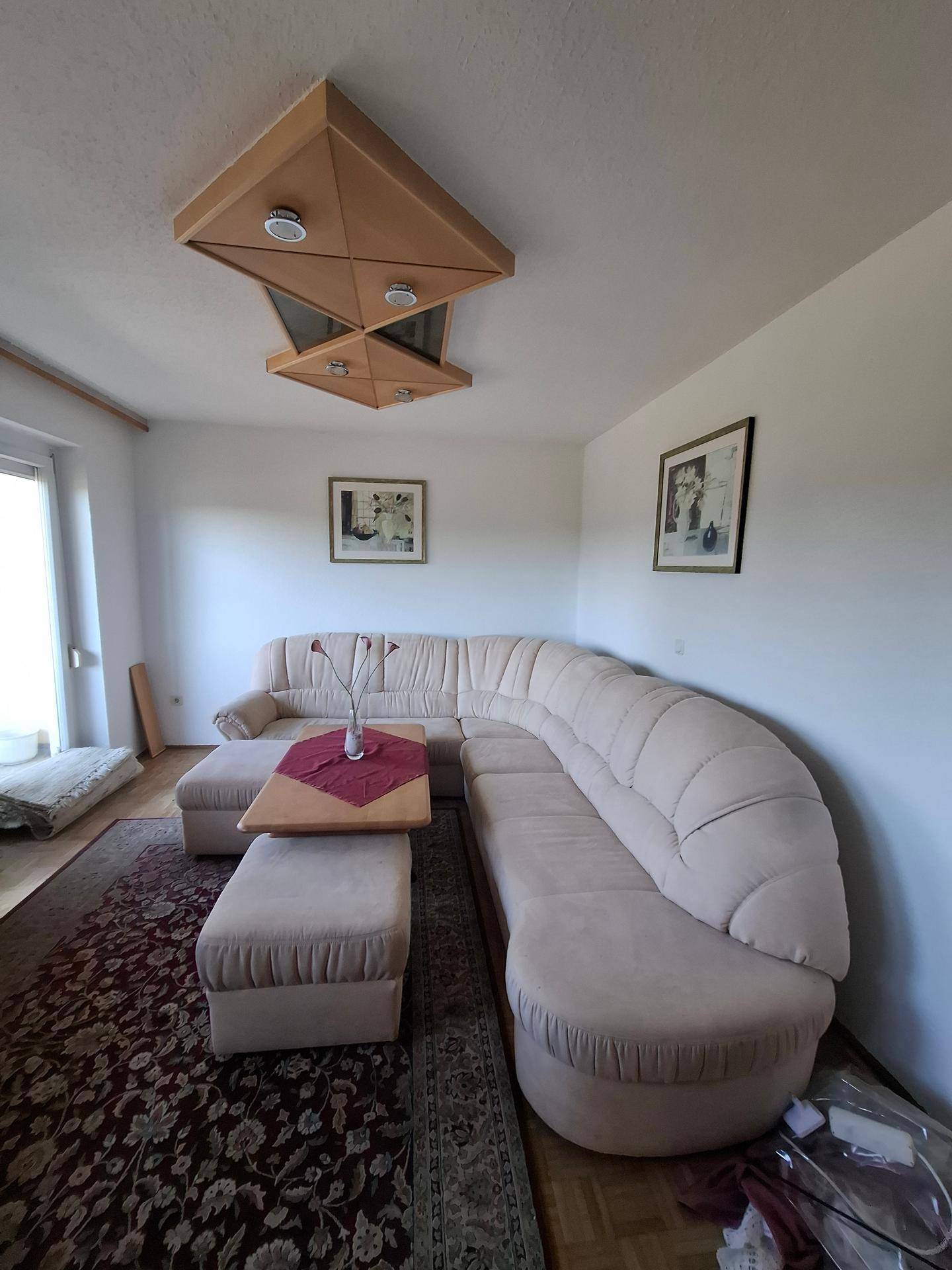 Gemütliches Wohnzimmer mit großer Eckcouch, Teppich und Holzboden, gut beleuchtet.