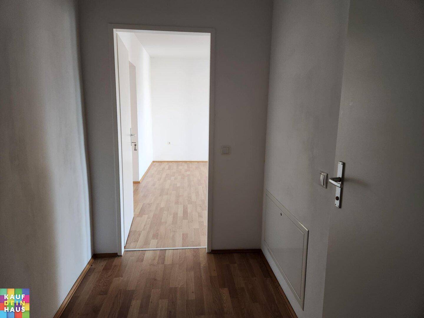 Heller Flur mit Laminatboden, der in einen weiteren leeren Raum führt.