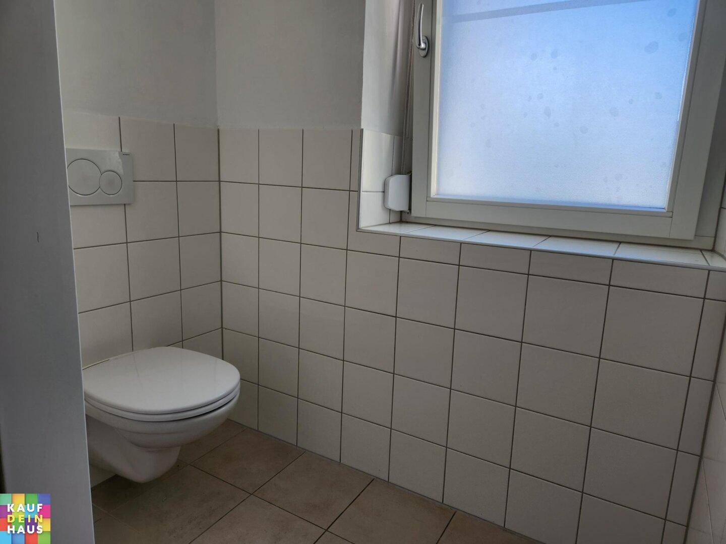Gäste-WC mit weißen Fliesen, wandhängendem WC und einem Fenster für Tageslicht.