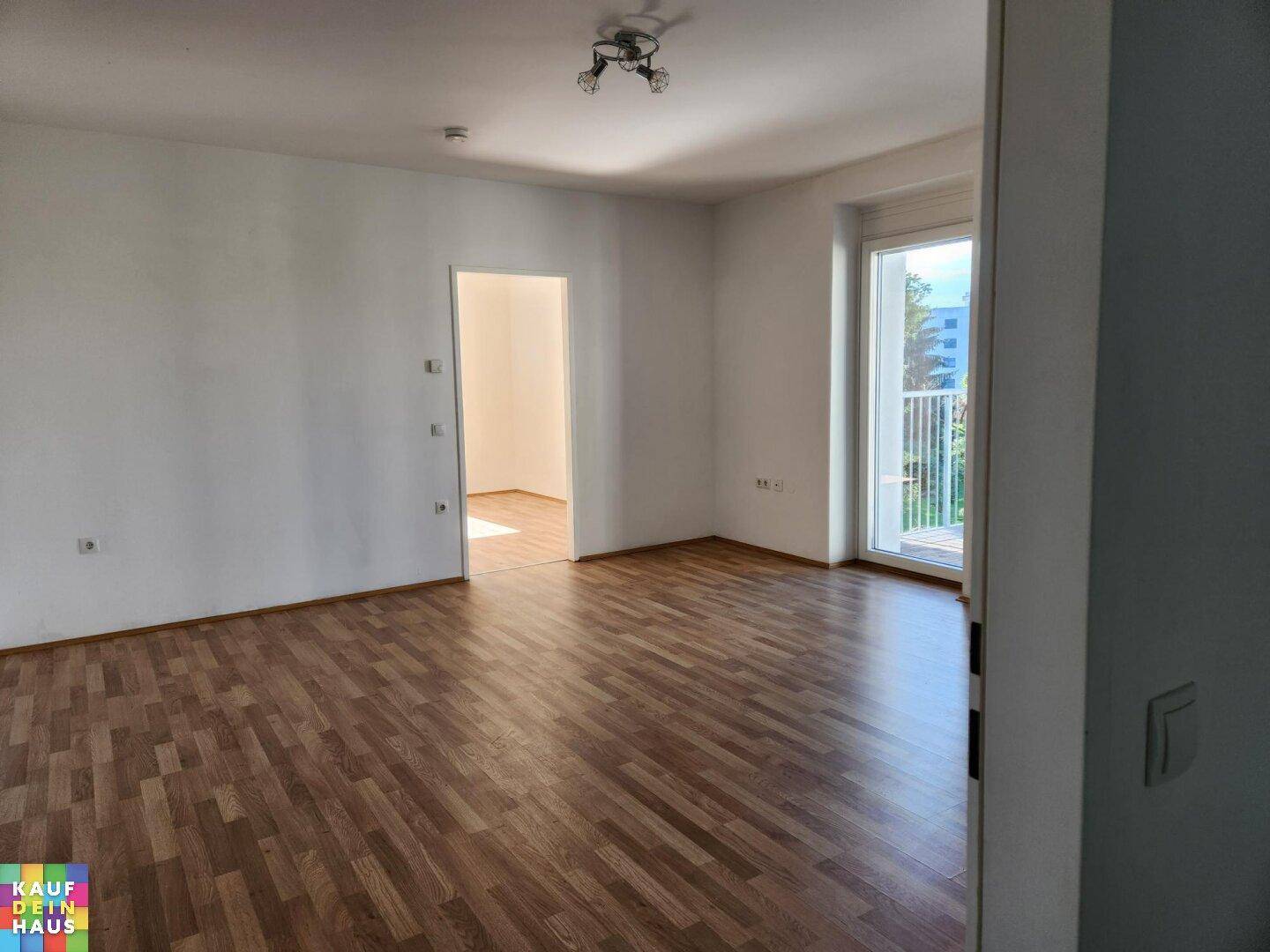 Geräumiges, leeres Wohnzimmer mit Laminatboden und Zugang zu einem Balkon.
