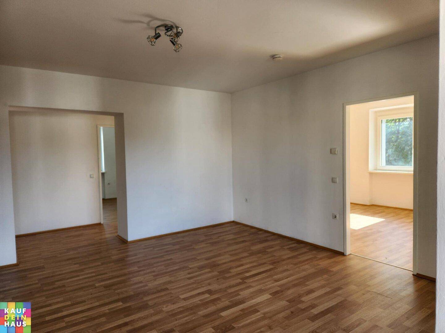 Helles Wohnzimmer mit Laminatboden und mehreren Türöffnungen zu angrenzenden Räumen.