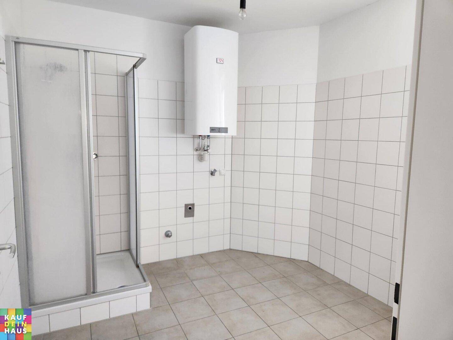 Badezimmer mit Duschkabine, weißen Fliesen und einem Warmwasserboiler an der Wand.