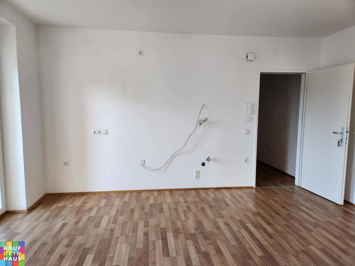 Leerer Raum mit Laminatboden und Anschlüssen für eine zukünftige Küche.