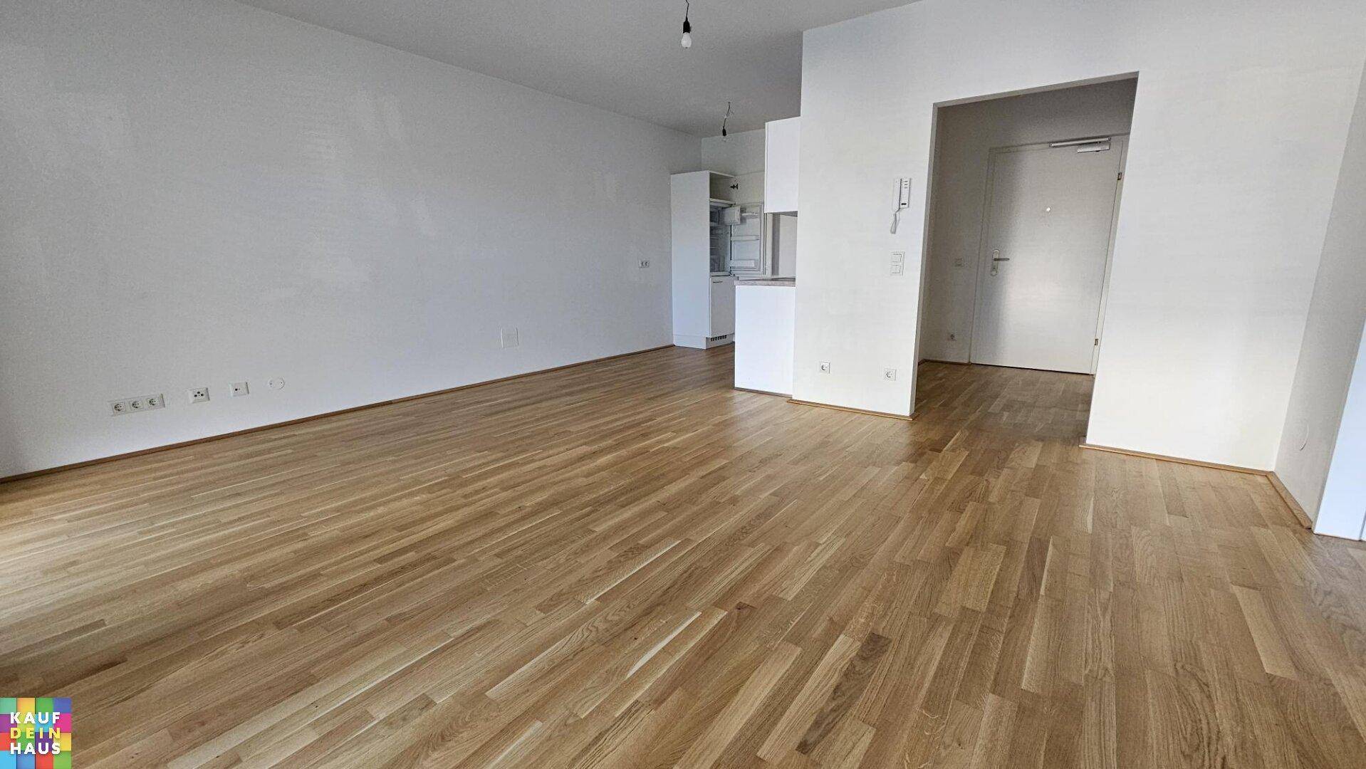 Geräumiger Wohnbereich mit Holzboden, weißen Wänden und offener Gestaltung zum Eingangsbereich.