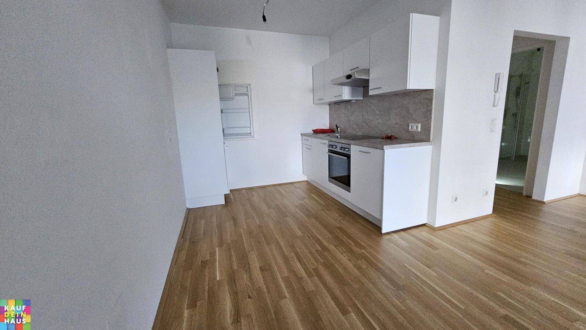 Moderne Küchenzeile mit weißen Schränken, integriertem Ofen und Holzboden in offener Raumgestaltung.
