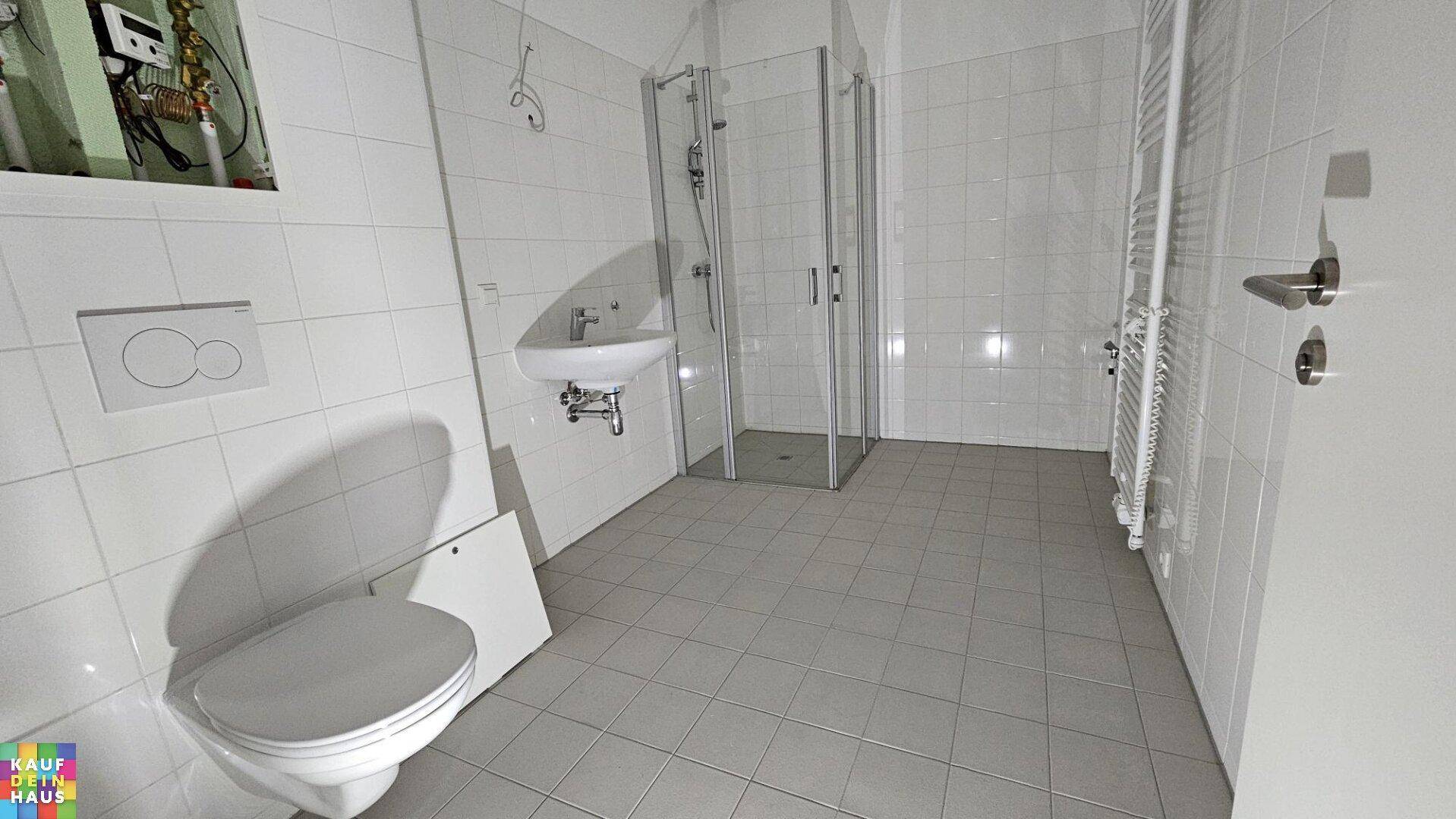 Modernes Badezimmer mit Dusche, WC, Waschbecken und weiß gefliesten Wänden und Boden.