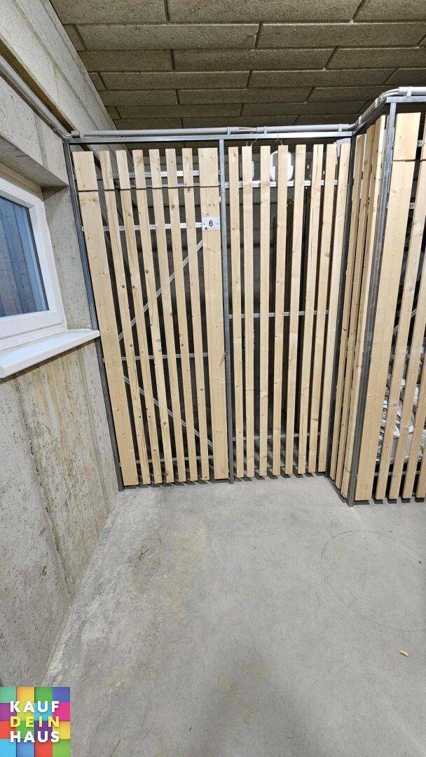 Kellerabteil mit Holzlattenwänden und Betonboden für zusätzlichen Stauraum.