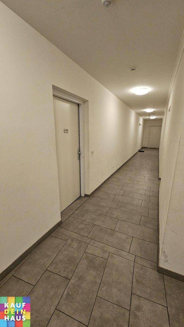Langer, sauberer Flur im Gebäude mit Fliesenboden und mehreren Türen.