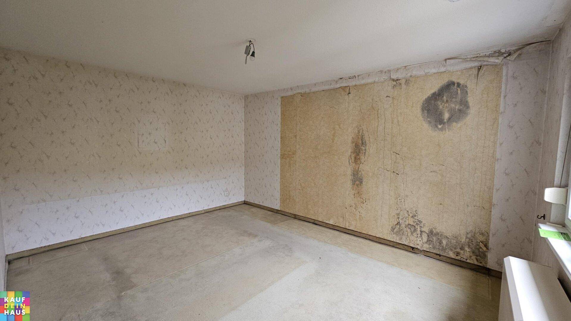 Leeres Zimmer mit abgenutzter Tapete und Spuren von Feuchtigkeit, bereit für eine Sanierung.