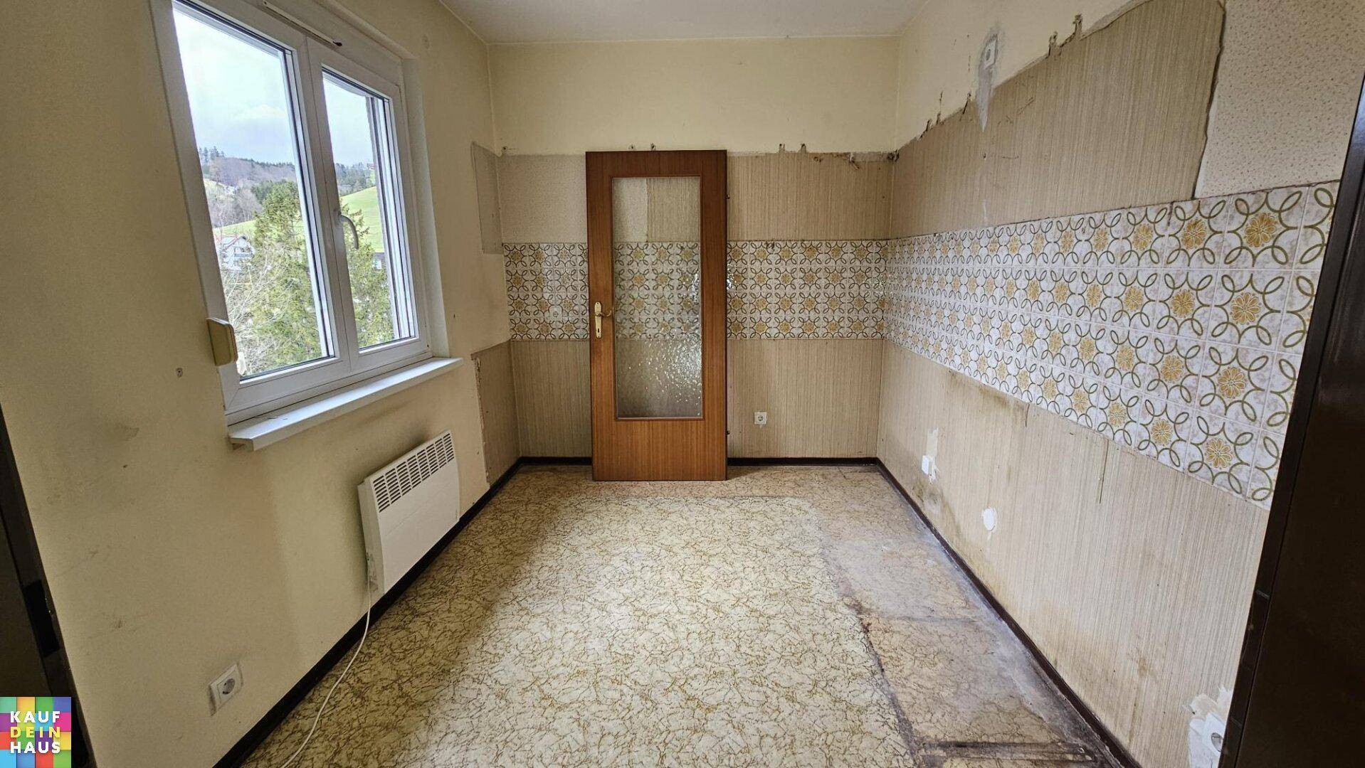 Zimmer mit Fenster, gemusterter Tapete und Linoleumboden, das eine umfassende Renovierung benötigt.