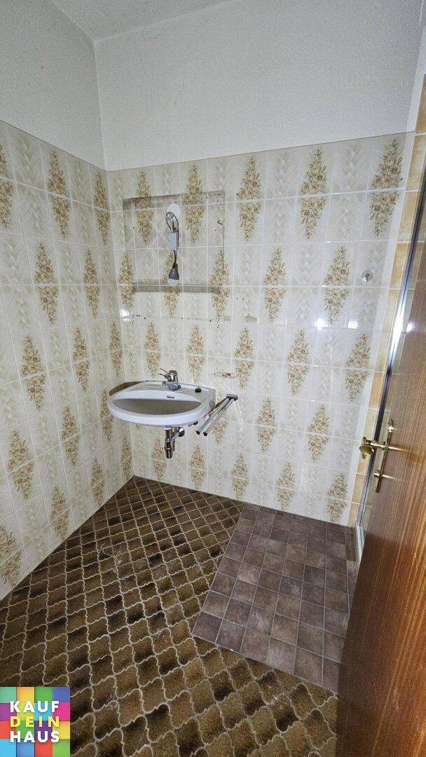 Badezimmer mit Waschbecken und gemusterten Fliesen an Wänden und Boden, im Stil der 80er Jahre.