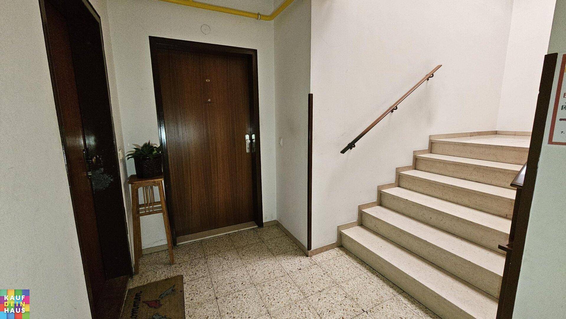 Treppenhaus im Eingangsbereich mit gefliestem Boden und Holzgeländer, das zu den oberen Etagen führt.