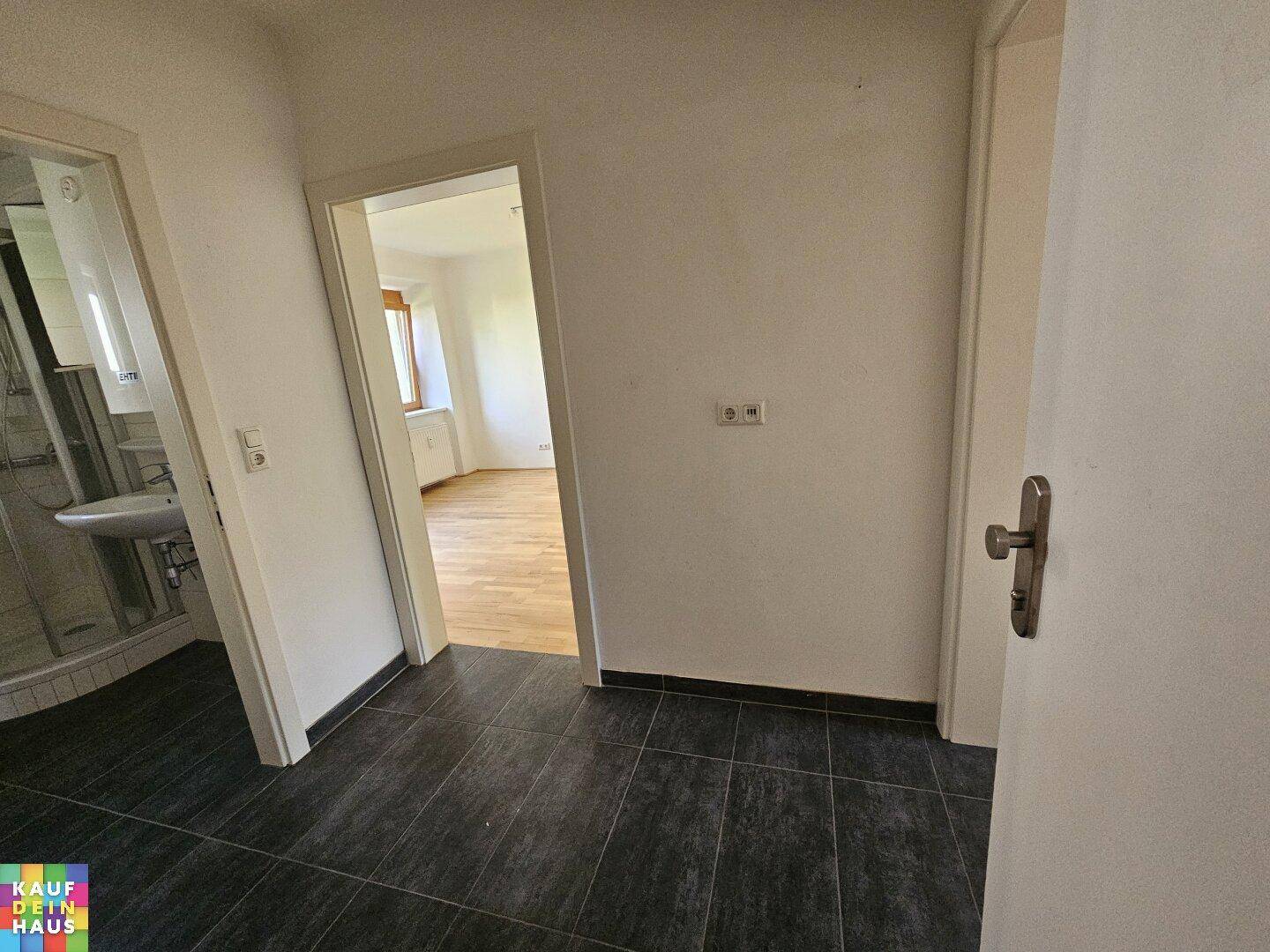 Flur mit dunklen Fliesen, der zu einem Badezimmer und einem weiteren Raum führt.