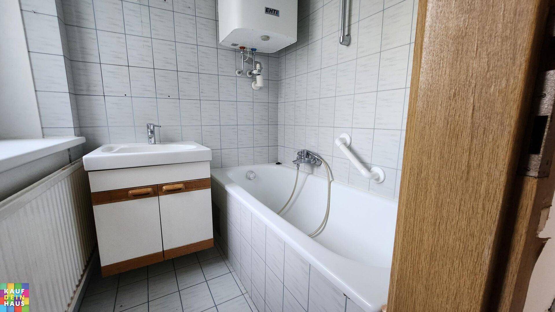Badezimmer mit Badewanne, Waschbecken und Fliesen, ausgestattet mit Haltegriffen für Sicherheit.