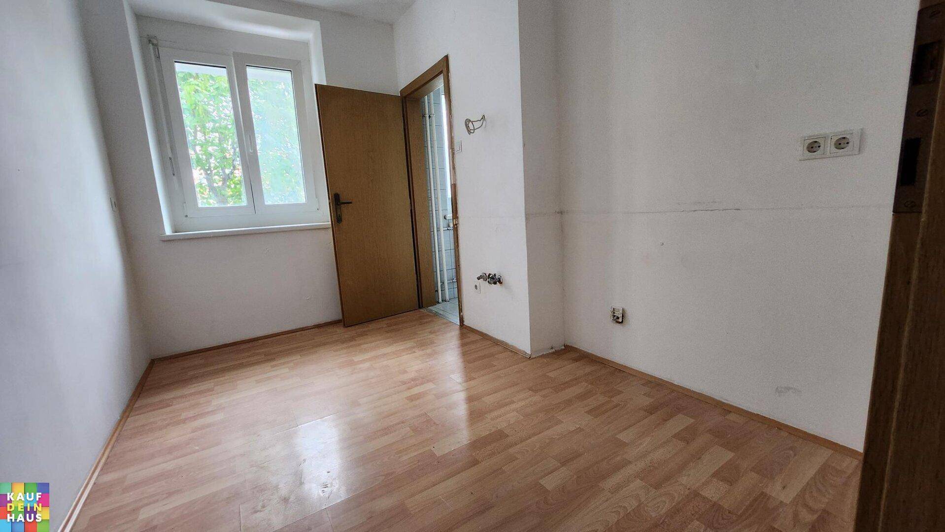 Leeres Zimmer mit Laminatboden und Fenster, bereit für neue Bewohner und Möbel.