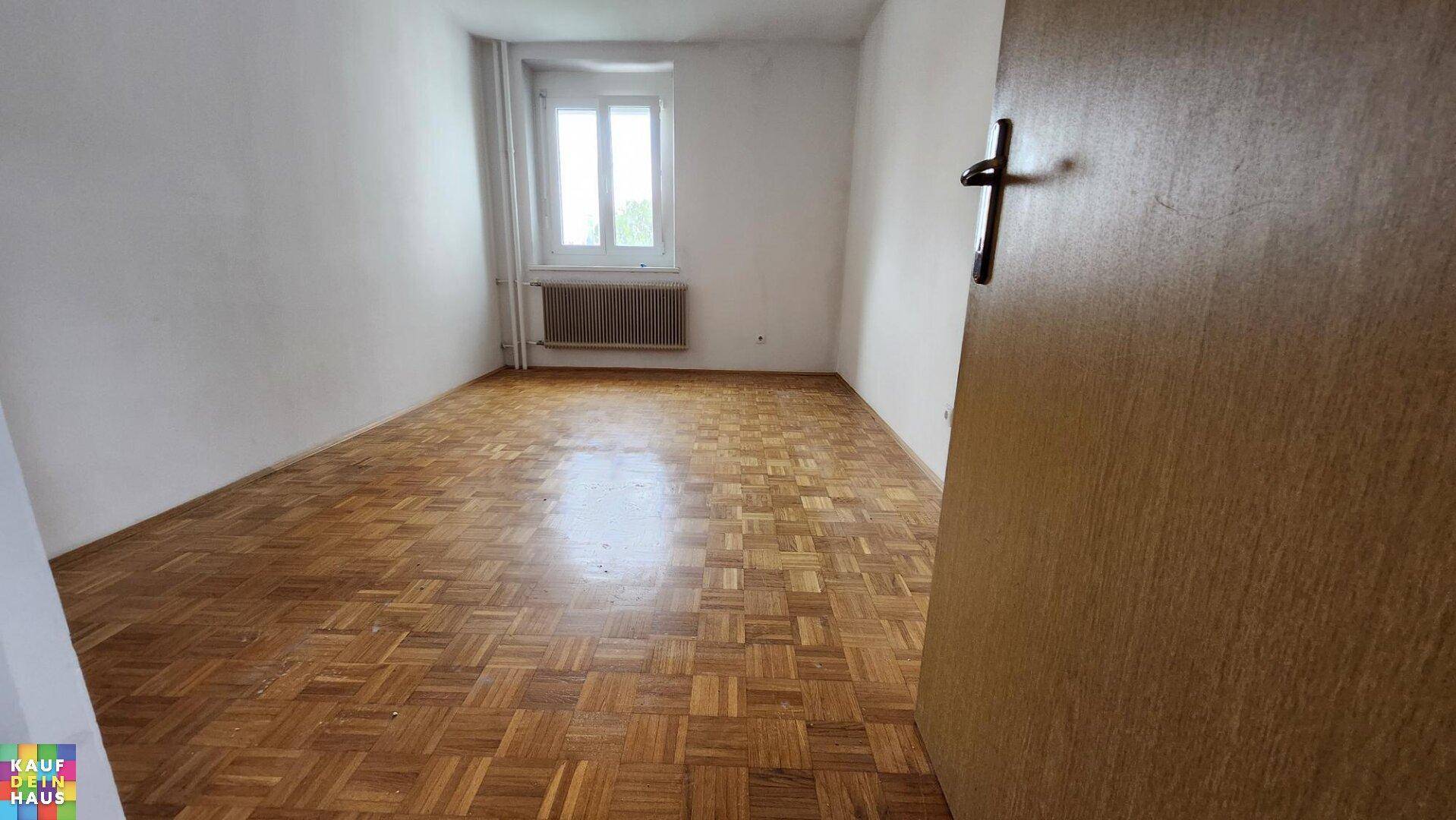 Helles Zimmer mit klassischem Parkettboden und Fenster, ideal als Wohn- oder Schlafbereich.