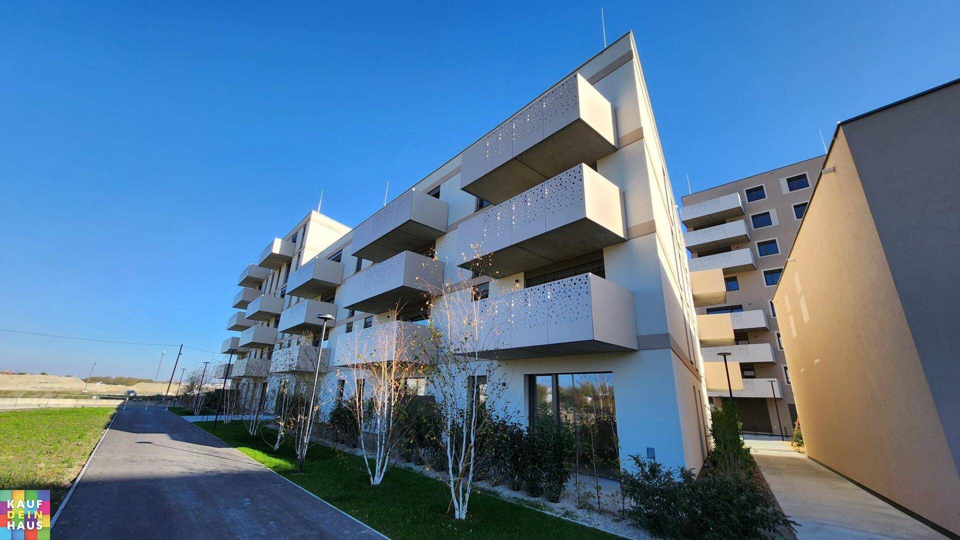 Moderne Wohngebäude mit markanten Balkonen und gepflegten Grünflächen unter blauem Himmel.
