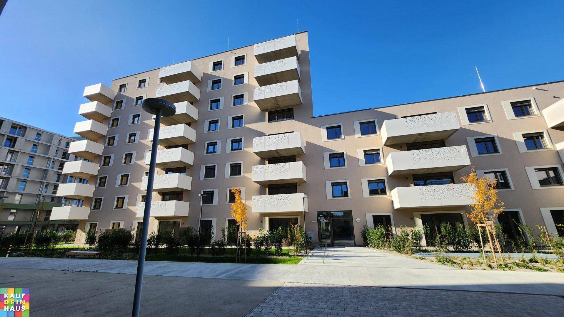 Moderne Wohngebäude mit zahlreichen Balkonen und gepflegten Grünflächen unter blauem Himmel.