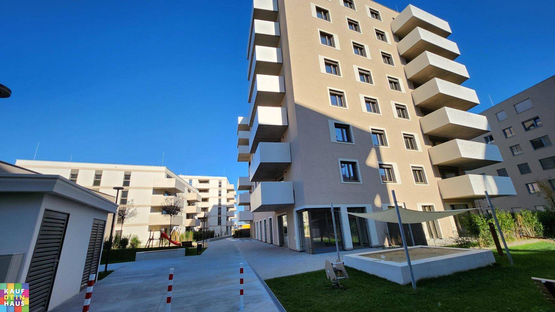 Moderne Wohnanlage mit Spielplatz, Sandkasten und gepflegten Grünflächen unter blauem Himmel.