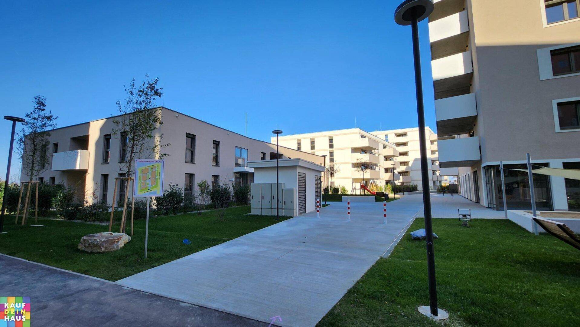 Moderne Wohngebäude mit gepflasterten Wegen und Grünflächen unter strahlend blauem Himmel.