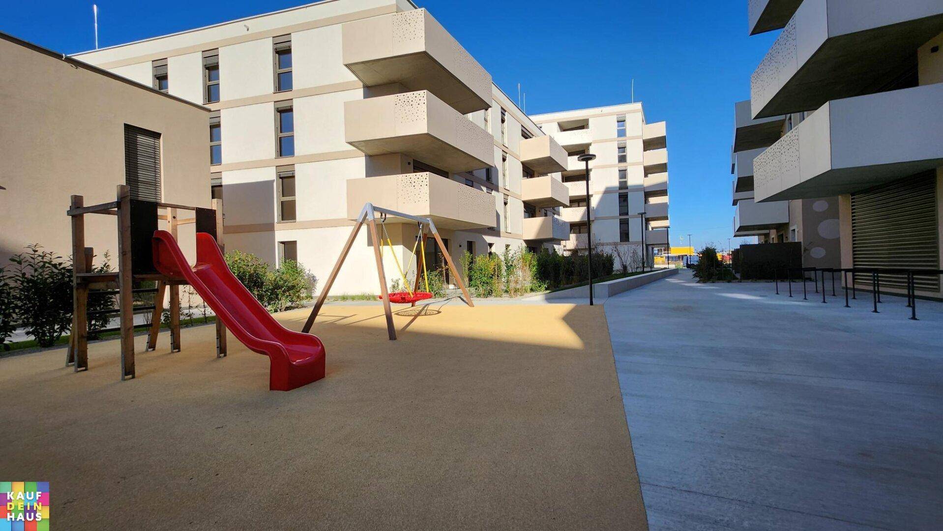 Moderne Wohnanlage mit Spielplatz, Rutsche und Schaukeln zwischen den Gebäuden.