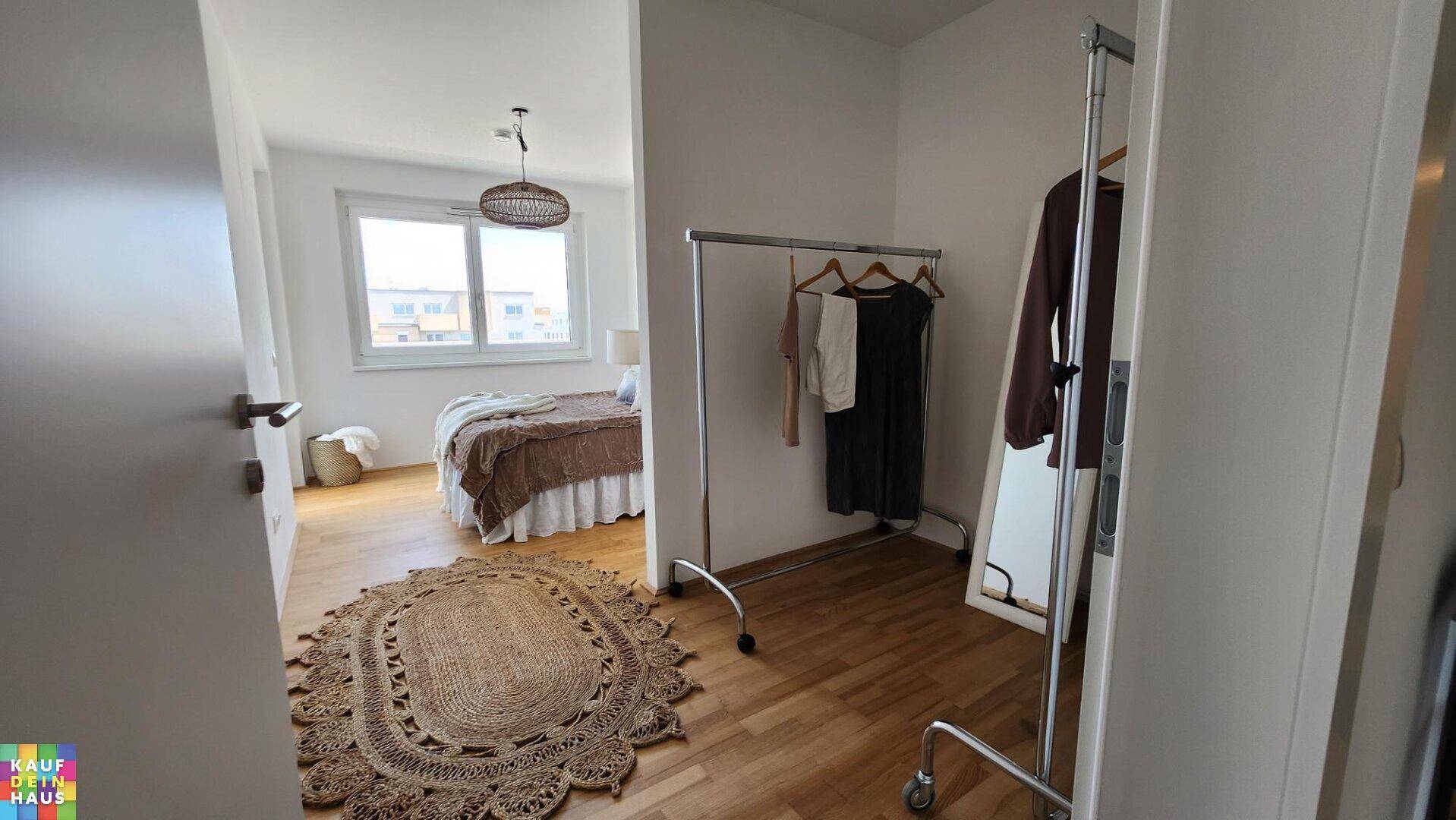 Schlafzimmer mit Holzboden, großem Fenster und einem Kleiderständer.
